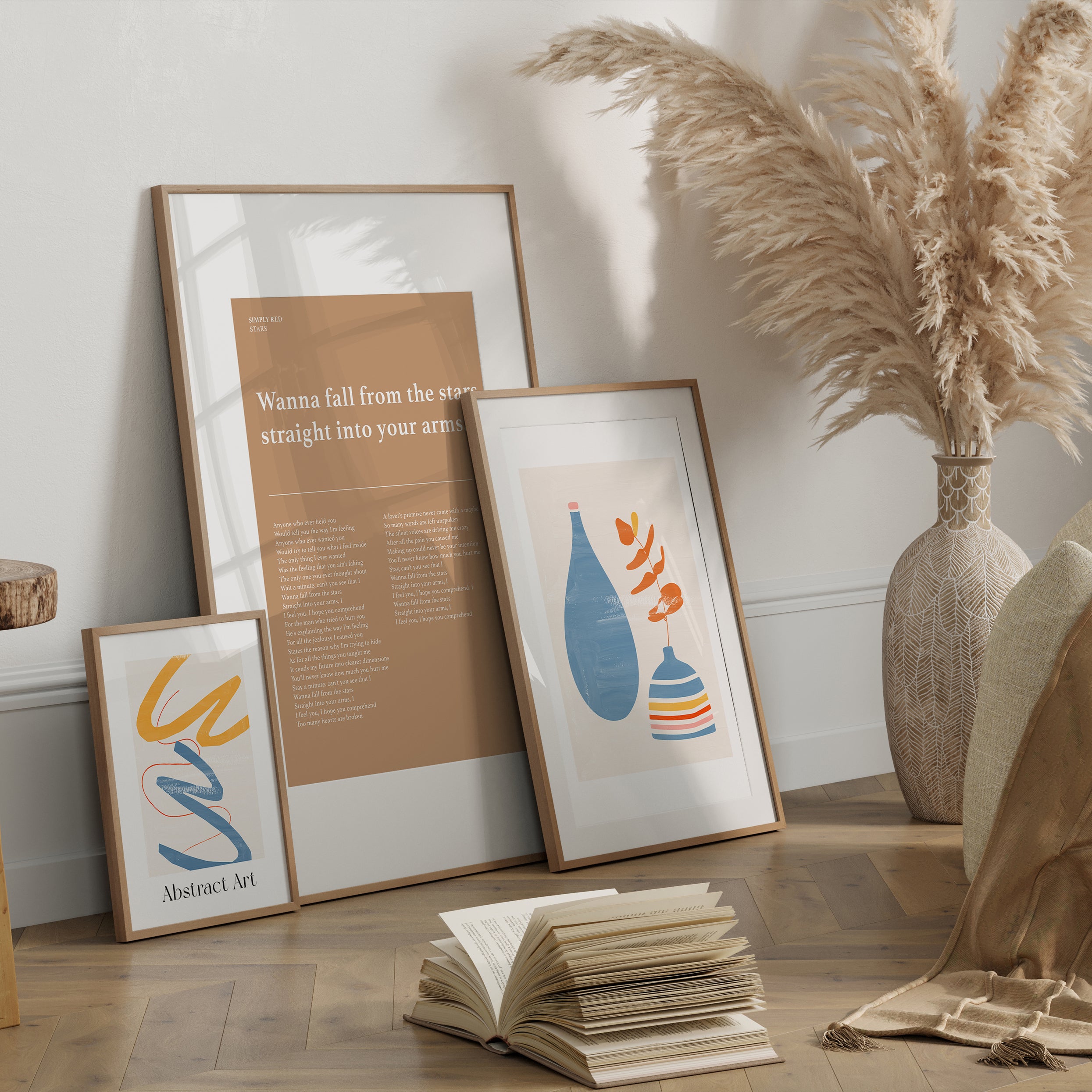 Framed abstract art pieces on a wooden floor with an open book and decorative vase.